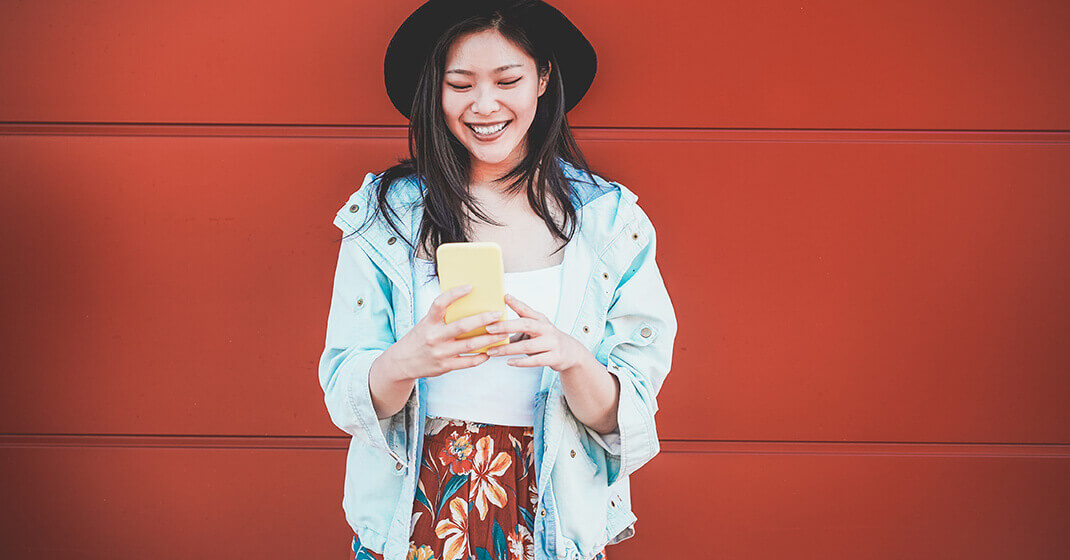 girl standing against red wall searching for salon marketing ideas on phone